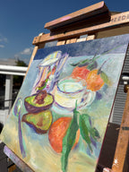 Angled detail image of an oil painting of an impressionist style still life with a shiny pitcher, halved avocado, cup of milk, and oranges.